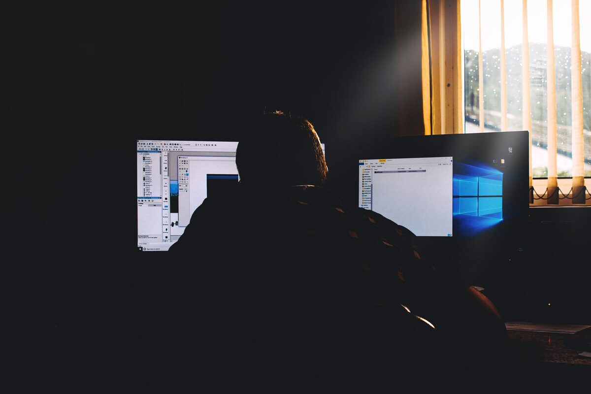 Sylwetka osoby przy dwóch monitorach z systemem Windows