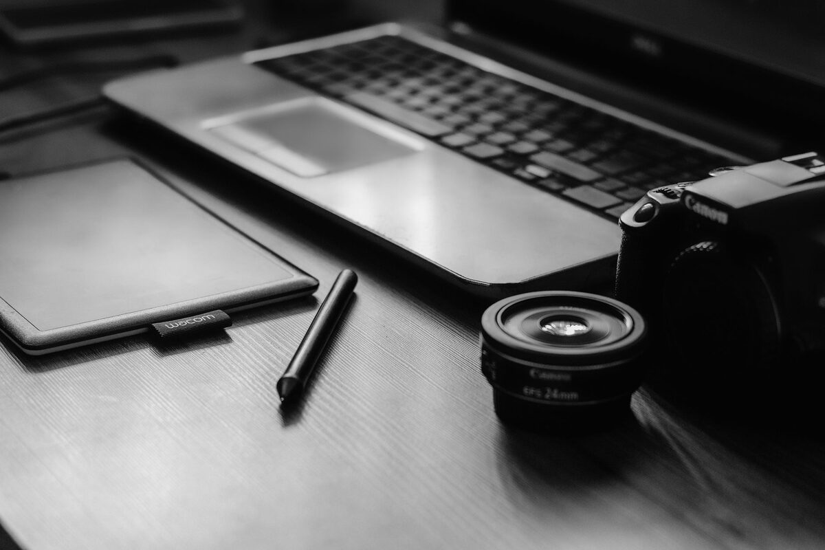 Laptop, telefon i obiektyw aparatu na biurku w czerni i bieli